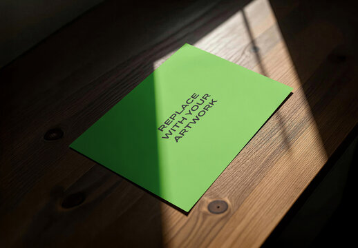 Rectangular poster mockup on a wooden surface with diagonal sunlight, realistic print presentation in an interior office or studio environment, template for branding advertising display