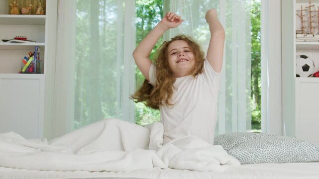 Good morning with child stretching in bed. Happy good morning with soft white bedding. Good morning routine in bright bedroom. Smiling child enjoys good morning beside window.