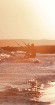 Kitesurfer carving through the waves with a kite against a glowing sunset