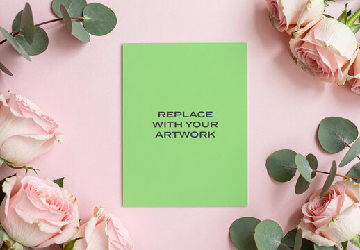 Vertical paper mockup with replace your artwork text centered on a pink surface, flat lay stationery presentation roses and eucalyptus leaves, floral arrangement, template