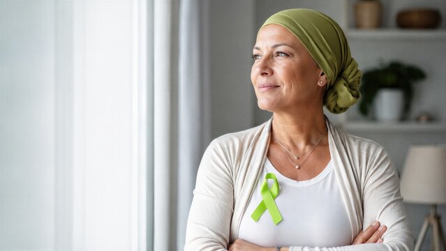 Woman cancer survivor wearing headscarf and green awareness ribbon at home. Lymphoma support, hope, treatment recovery and World Lymphoma Awareness Day concept with copy space.
