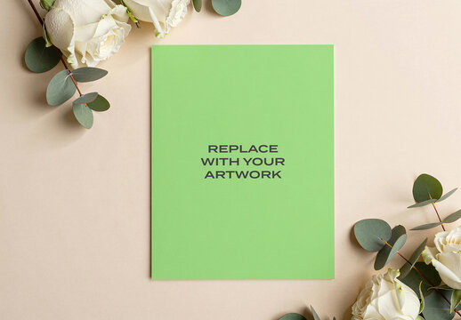 Vertical poster mockup displayed on a beige surface with white roses and eucalyptus, realistic print presentation in flat lay composition, stationery branding template