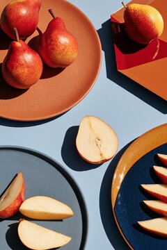 Overhead still life composition of ripe red and yellow pears on colorful ceramic plates on pale blue surface for food background and modern tableware poster