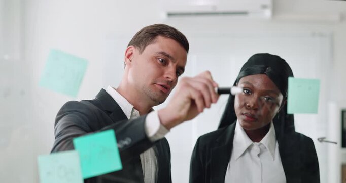 Portrait of African American woman with man colleague works on business strategy at glass board in office. Professionals share solutions of growth in boardroom