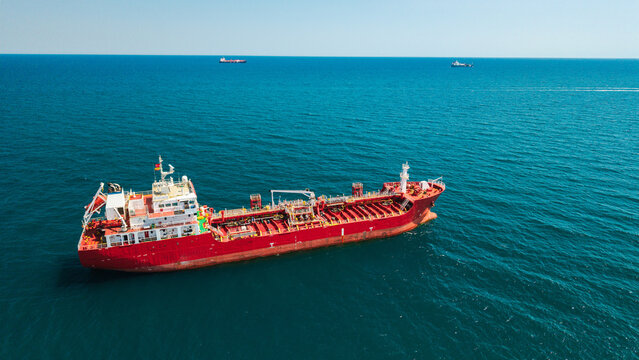 Aerial view of red tanker ship anchored in calm blue sea with distant cargo vessels