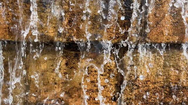 Clear fountain water splashes continuously across a weathered stone wall