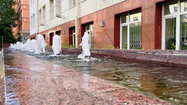 Granite city fountain sends bubbling water jets beside a modern building