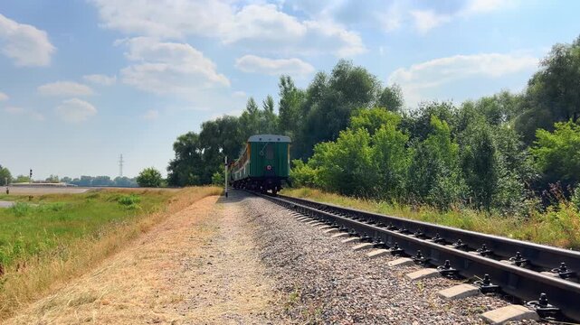 Small narrow gauge train travels away through a rural landscape