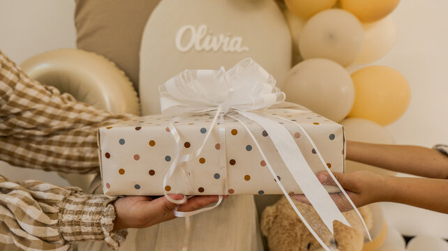 Hands exchanging a polka dot gift box with a large white bow, celebrating a special occasion