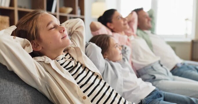 Family parents and children relaxing together on sofa. Cozy home interior with soft light and comfortable couch, showing weekend leisure, happiness and joy. Family relaxing at home concept.