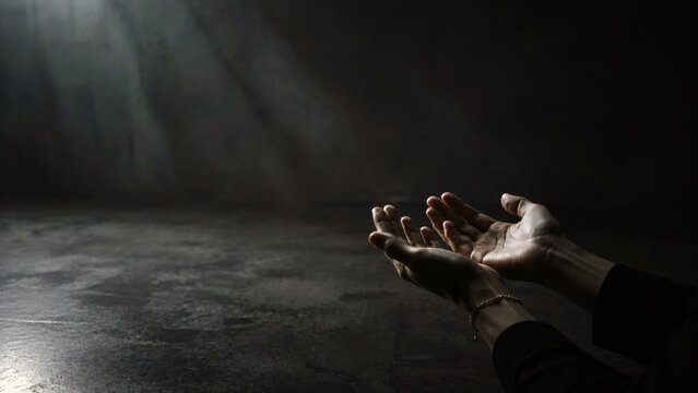 Open hands reaching toward light in a dark space, symbolizing hope, help, faith, support and emotional recovery during difficult times