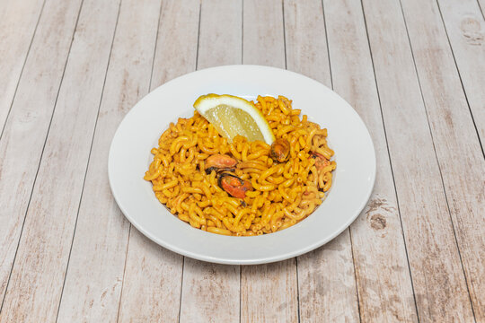 Spanish Fideu&agrave; with Mussels and Lemon Wedge Served on White Plate on Wooden Table