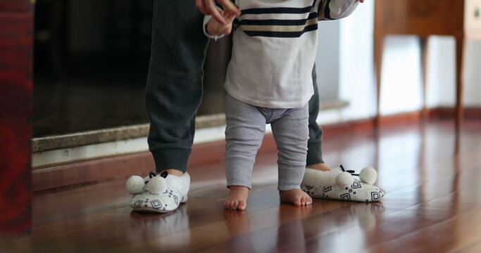 Baby learning to walk. Mother helping toddler infant to stand-up indoor