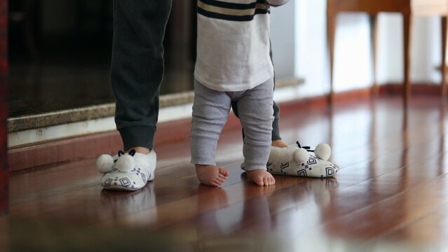 Baby learning to walk. Mother helping toddler infant to stand-up indoor
