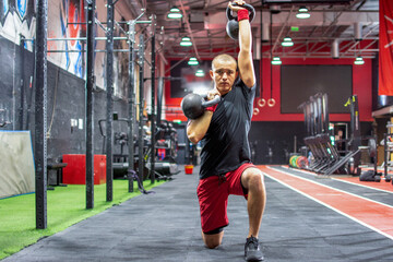 Fototapeta premium Focused young man performing a kneeling kettlebell press exercise at gym