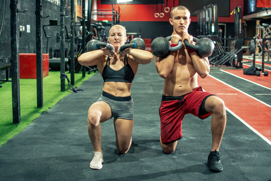 Athletic couple performing synchronized kettlebell front rack lunges at gym