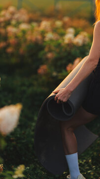 Woman holding a rolled yoga mat outdoors in golden hour light