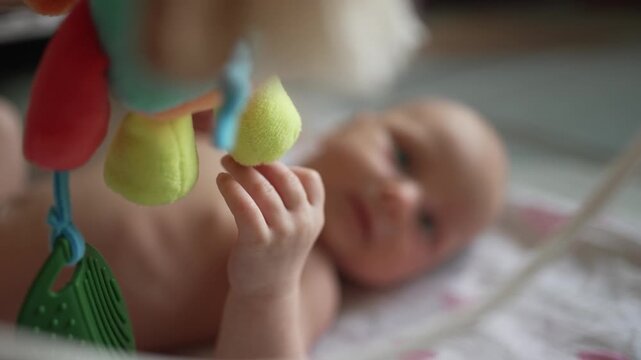 Adorable newborn baby with blue eyes lying in a crib and watching a colorful mobile toy, an infant actively developing sensory skills and exploring the world around them for the first time