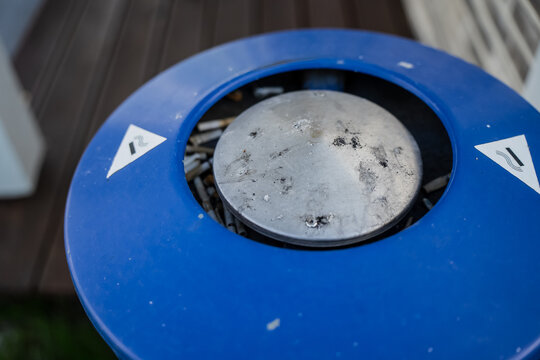 Public designated smoking area outdoor blue metal ashtray bin filled with discarded cigarette filters highlighting smoking habits and littering