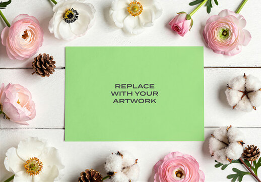 Rectangular card mockup displayed on a white wooden surface surrounded by pink and flowers, cotton bolls, pinecones, Template, flat lay stationery branding presentation with natural light