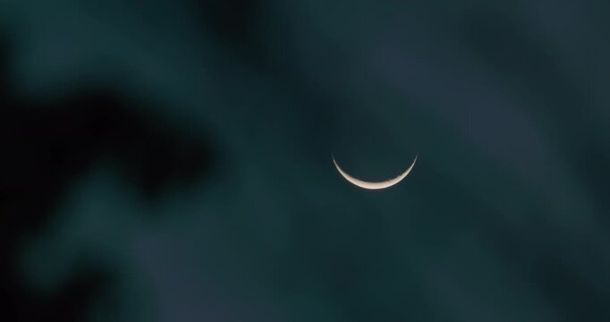 Slender crescent moon glowing in twilight sky with soft moody clouds drifting by. Minimalist tranquil scene for nature, mindfulness, and atmospheric transitions.