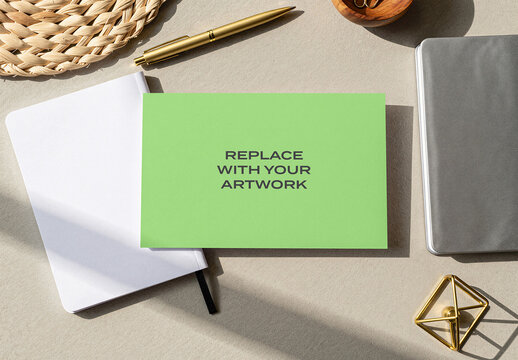 Rectangular card mockup displayed on a light textured surface with white notebook, gold pen, and gray arranged in flat lay composition for branding presentation print display