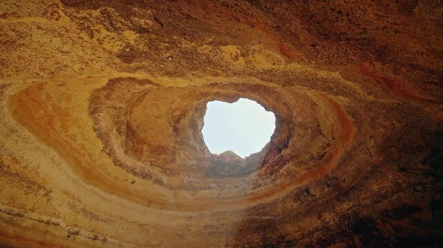 Circular ceiling opening illuminates the layered limestone interior of Benagil Cave on the Algarve coast of Portugal.