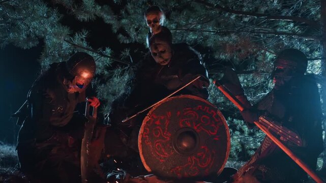 Three armed warriors crouch around glowing campfire in moonlit forest, tending flames while keeping watch, spears ready, firelight revealing tense faces, drifting smoke, and misty shadows among trees