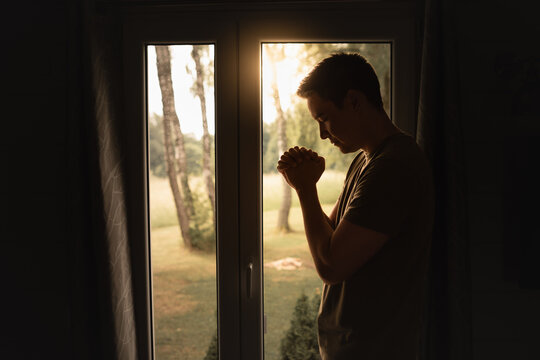 Religious worship, and spiritual enlightenment concept. man saying a prayer next to window at sunrise.	