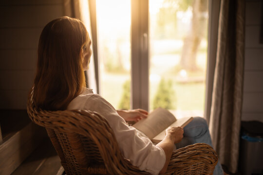 Woman at home relaxing by the window reading and enjoying a morning weekend day off 	