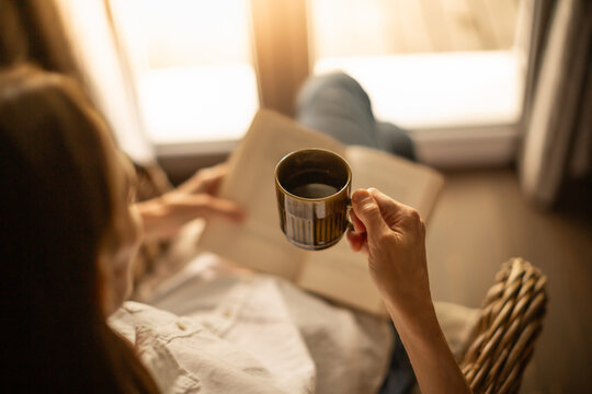 Person at home relaxing by the window reading and enjoying a morning cup of coffee	