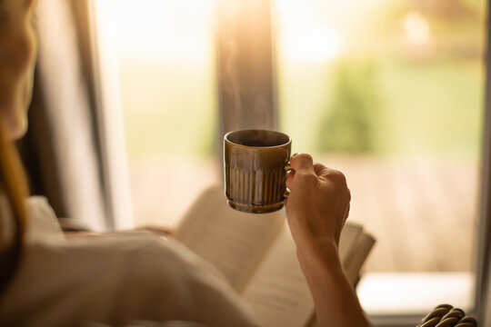 Person relaxing at home reading book feeling relaxed on a cozy winter morning enjoying cup of hot tea coffee	
