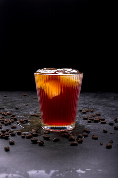 Refreshing iced coffee cocktail with orange slice ice cubes vintage manual grinder and scattered roasted coffee beans on dark surface
Keywords