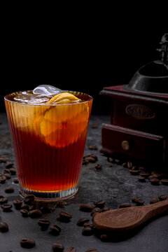 Refreshing iced coffee cocktail with orange slice ice cubes vintage manual grinder and scattered roasted coffee beans on dark surface
Keywords