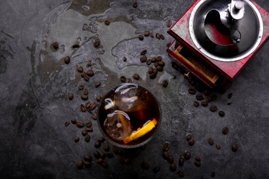 Refreshing iced coffee cocktail with orange slice ice cubes vintage manual grinder and scattered roasted coffee beans on dark surface
Keywords