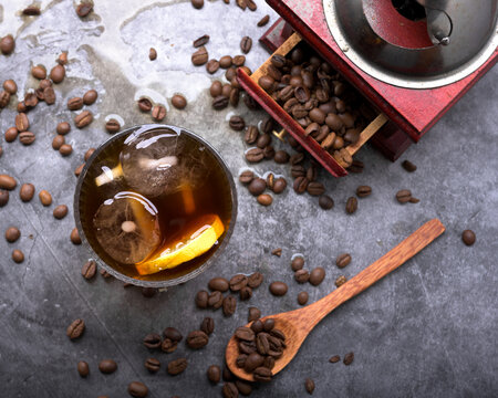Refreshing iced coffee cocktail with orange slice ice cubes vintage manual grinder and scattered roasted coffee beans on dark surface
Keywords