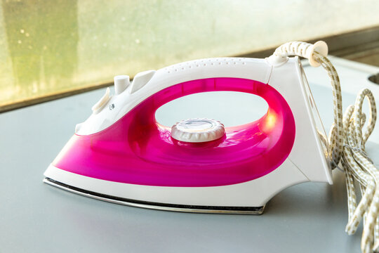 Modern Electric Steam Iron with Pink Water Tank on Grey Surface