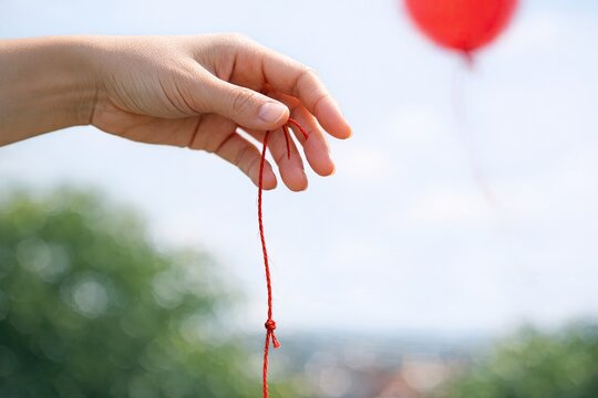A person's hand holding a string with a red balloon in the background