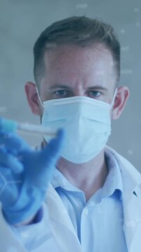 Animation of chemical structures over caucasian male doctor holding vaccine wearing face mask