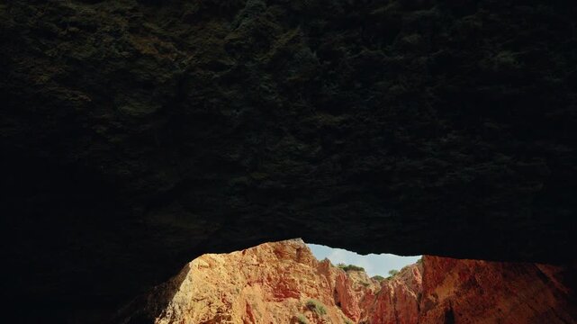 Dark limestone ceiling and sunlit golden cliffs viewed from inside Gruta do Paraiso near Carvoeiro, Portugal.