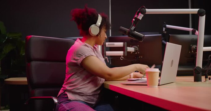 African American woman with headset typing on laptop in studio, adjusting mic, preparing to record