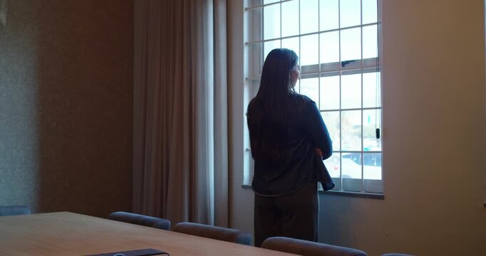 African American woman pausing hands-on-hips fixing jacket gazing out window past table, copy space