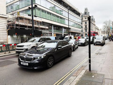 Busy London, UK city street traffic with BMW i5 cars queued by construction and historic buildings