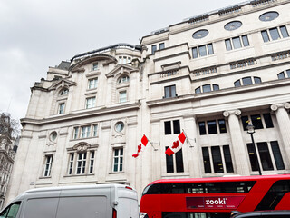 Fototapeta premium Canadian flags flying on a historic government building Oceanic House facade with red bus in London, UK Cockspur street