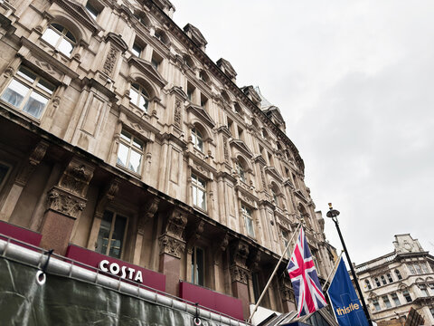 Historic ornate building with Costa cafe and flags outside Thistle hotel in London, UK