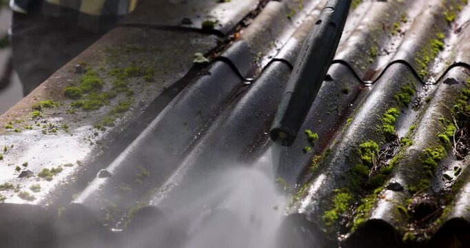 Washing dirt and moss from house corrugated roofing sheets with high pressure washer. Roof cleaning service