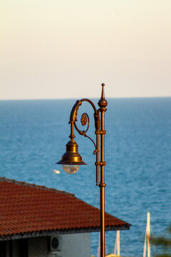 Vertical eye level medium shot of a vintage bronze street lamp against a sea horizon background
