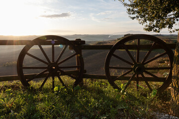 Fototapeta premium Old wooden wheels lean against a fence in a Tuscan landscape