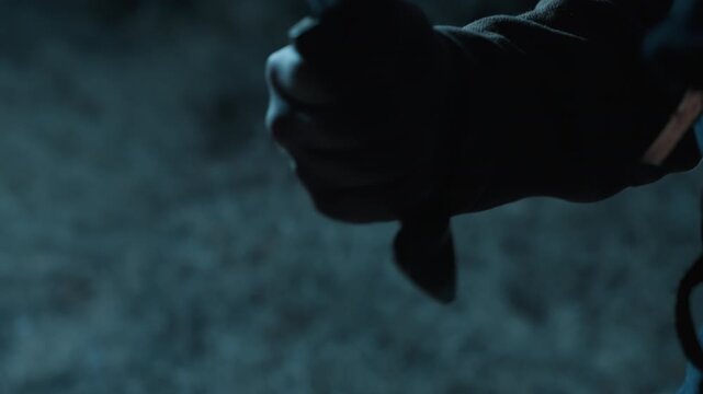 Tight diagonal close view of forearm and hand gripping sword hilt during swing, with tense posture, angled blade, cool blue lighting, dark shadows, and rough stone backdrop, with hand, arm, sword