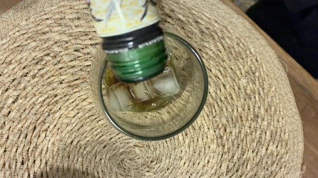 Pouring dark aromatic Fernet liqueur into a glass filled with ice cubes to prepare classic Argentine cocktail, night out